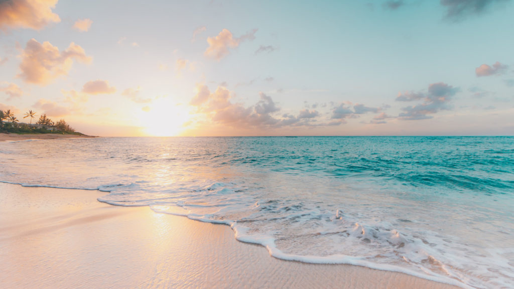 a beach at sunset with turquoise waters, waves rolling in and an expanse of beige sand.