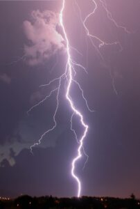 A bolt of lightning passes through dark blue & purple sky to reach the ground.