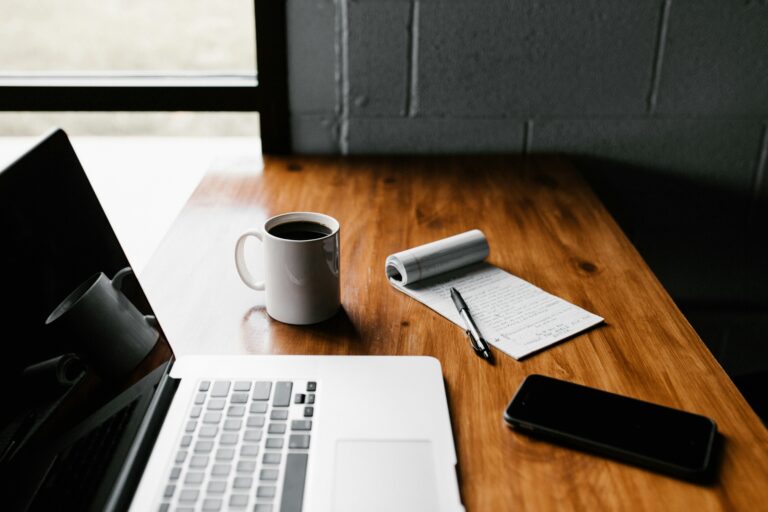A computer, cup of coffee, notepad and pen on a desk